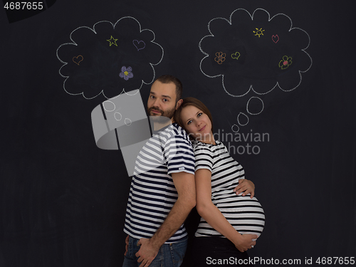 Image of pregnant couple posing against black chalk drawing board