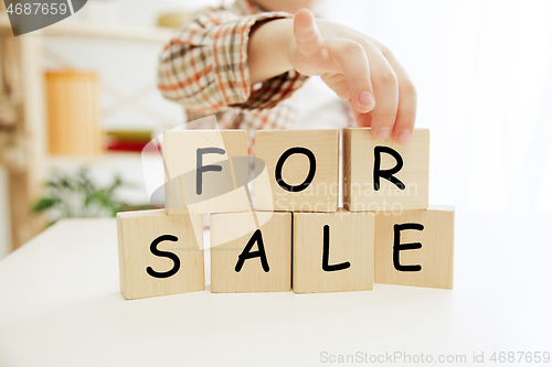 Image of Wooden cubes with words sale in hands of happy smiling little boy at home