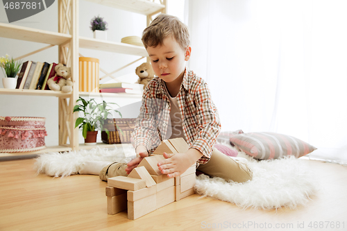 Image of Little child sitting on the floor. Pretty boy palying with wooden cubes at home