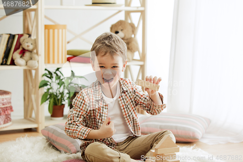 Image of Little child sitting on the floor. Pretty boy palying with wooden cubes at home