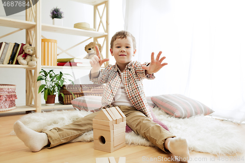 Image of Little child sitting on the floor. Pretty boy palying with wooden cubes at home