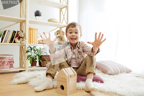 Image of Little child sitting on the floor. Pretty boy palying with wooden cubes at home