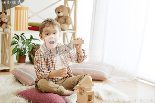 Image of Little child sitting on the floor. Pretty boy palying with wooden cubes at home