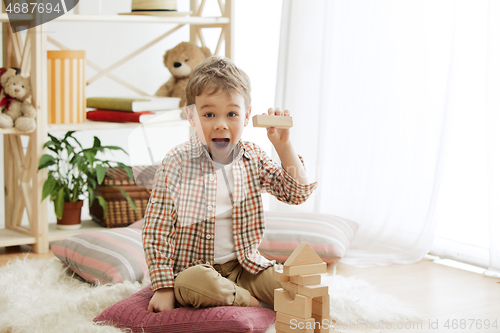 Image of Little child sitting on the floor. Pretty boy palying with wooden cubes at home