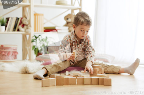 Image of Little child sitting on the floor. Pretty boy palying with wooden cubes at home