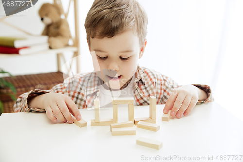 Image of Little child sitting on the floor. Pretty boy palying with wooden cubes at home