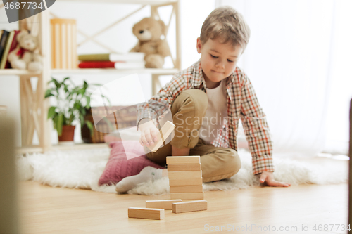 Image of Little child sitting on the floor. Pretty boy palying with wooden cubes at home