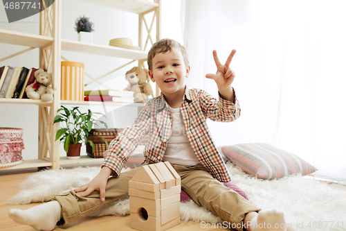 Image of Little child sitting on the floor. Pretty boy palying with wooden cubes at home