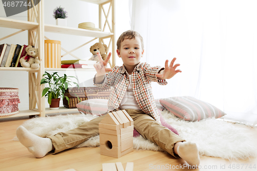 Image of Little child sitting on the floor. Pretty boy palying with wooden cubes at home