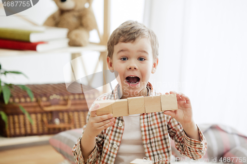 Image of Little child sitting on the floor. Pretty boy palying with wooden cubes at home