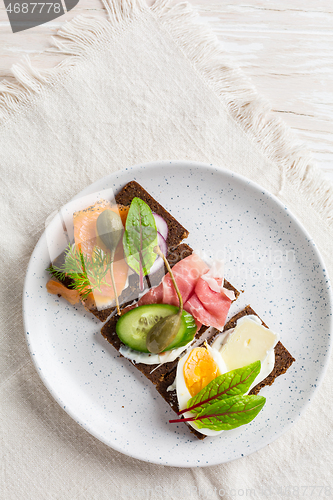 Image of Variation of healthy open sandwiches on Pumpernickel bread with vegetables, salmon, ham, herbs and soft cheese