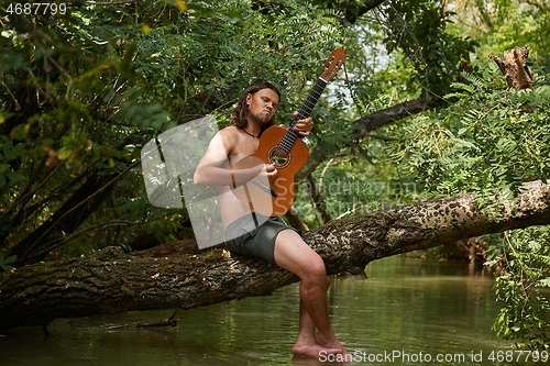 Image of Playing the guitar on a tree above a river