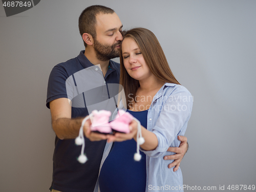 Image of pregnant couple holding newborn baby shoes