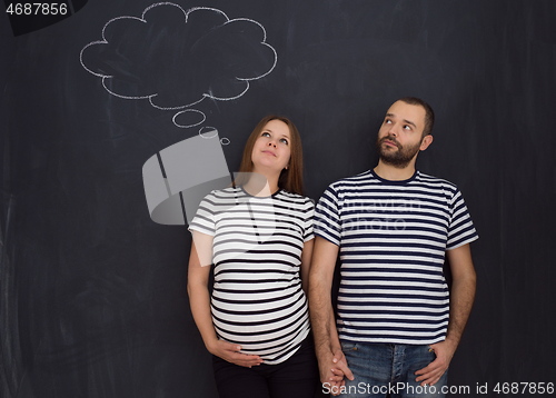 Image of pregnant couple posing against black chalk drawing board