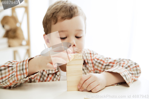 Image of Little child sitting on the floor. Pretty boy palying with wooden cubes at home