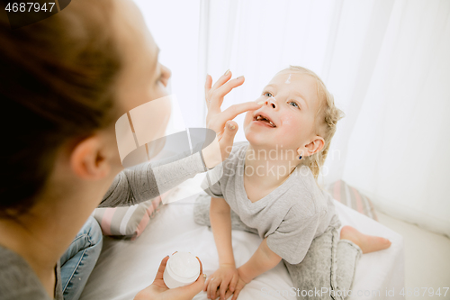 Image of Young mother and her little daughter hugging and kissing on bed