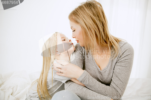 Image of Young mother and her little daughter hugging and kissing on bed