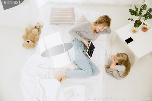 Image of Young mother and her little daughter hugging and kissing on bed