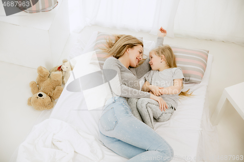 Image of Young mother and her little daughter hugging and kissing on bed