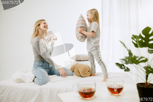 Image of Young mother and her little daughter hugging and kissing on bed