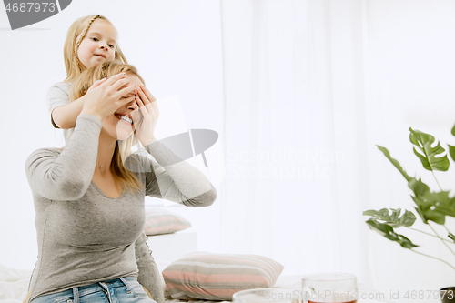 Image of Young mother and her little daughter hugging and kissing on bed