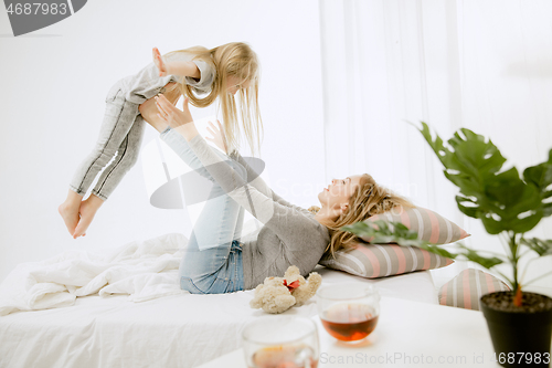 Image of Young mother and her little daughter hugging and kissing on bed