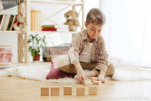 Image of Little child sitting on the floor. Pretty boy palying with wooden cubes at home