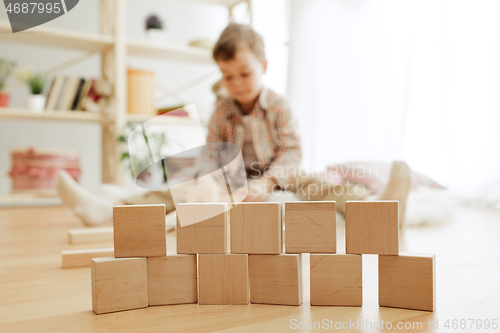 Image of Little child sitting on the floor. Pretty boy palying with wooden cubes at home