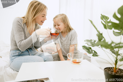 Image of Young mother and her little daughter hugging and kissing on bed