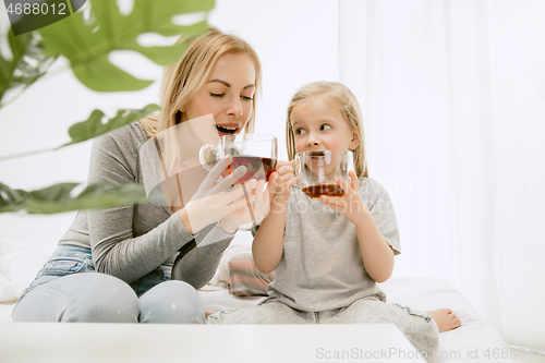 Image of Young mother and her little daughter hugging and kissing on bed