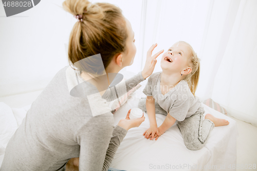 Image of Young mother and her little daughter hugging and kissing on bed