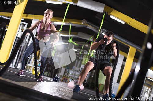 Image of sports couple doing battle ropes cross fitness exercise