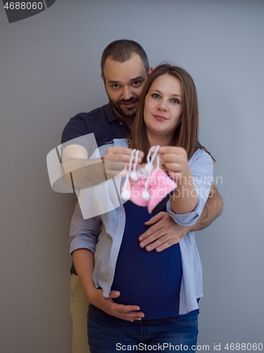 Image of pregnant couple holding newborn baby shoes