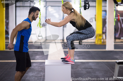 Image of woman working out with personal trainer jumping on fit box