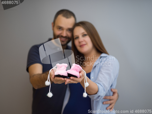 Image of pregnant couple holding newborn baby shoes