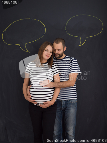 Image of pregnant couple posing against black chalk drawing board