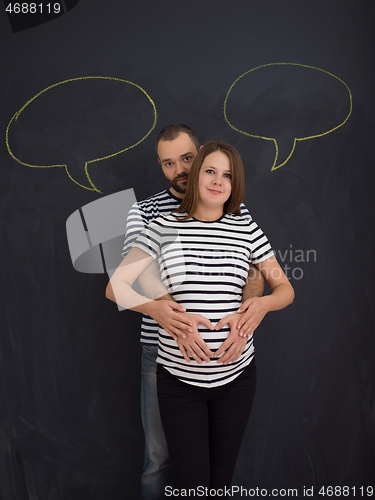 Image of pregnant couple posing against black chalk drawing board