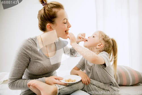 Image of Young mother and her little daughter hugging and kissing on bed