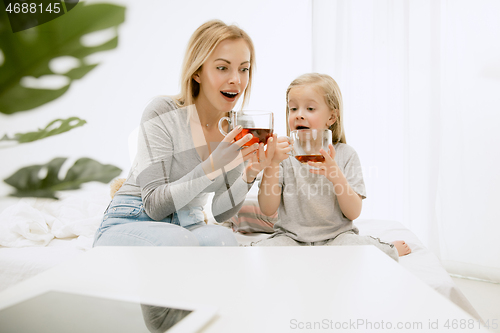 Image of Young mother and her little daughter hugging and kissing on bed