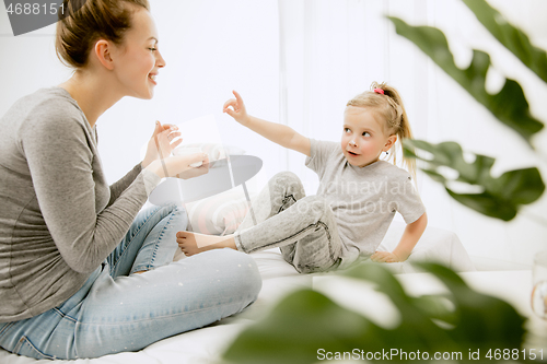 Image of Young mother and her little daughter hugging and kissing on bed