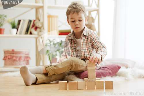 Image of Little child sitting on the floor. Pretty boy palying with wooden cubes at home