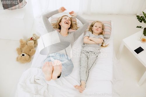 Image of Young mother and her little daughter hugging and kissing on bed