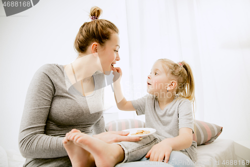 Image of Young mother and her little daughter hugging and kissing on bed