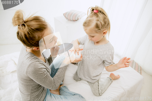 Image of Young mother and her little daughter hugging and kissing on bed