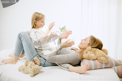 Image of Young mother and her little daughter hugging and kissing on bed