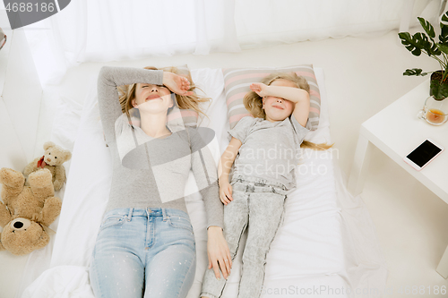 Image of Young mother and her little daughter hugging and kissing on bed