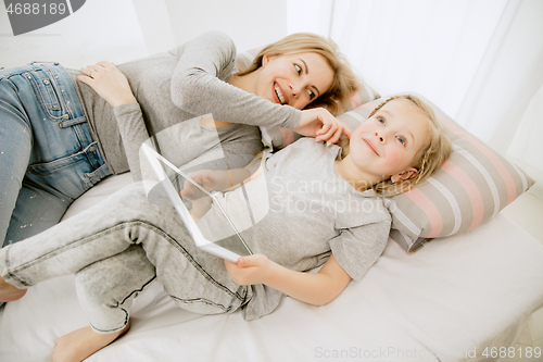 Image of Young mother and her little daughter hugging and kissing on bed