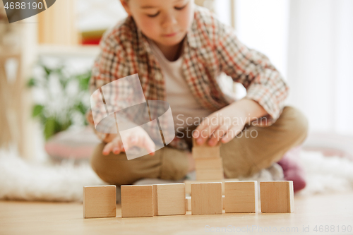 Image of Little child sitting on the floor. Pretty boy palying with wooden cubes at home