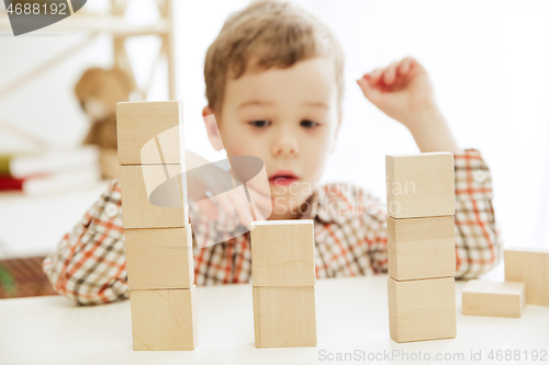 Image of Little child sitting on the floor. Pretty boy palying with wooden cubes at home