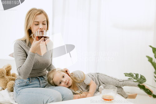 Image of Young mother and her little daughter hugging and kissing on bed